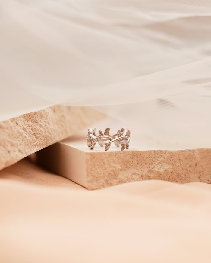 A detailed shot of an elegant silver ring on a stone block with a soft fabric backdrop.