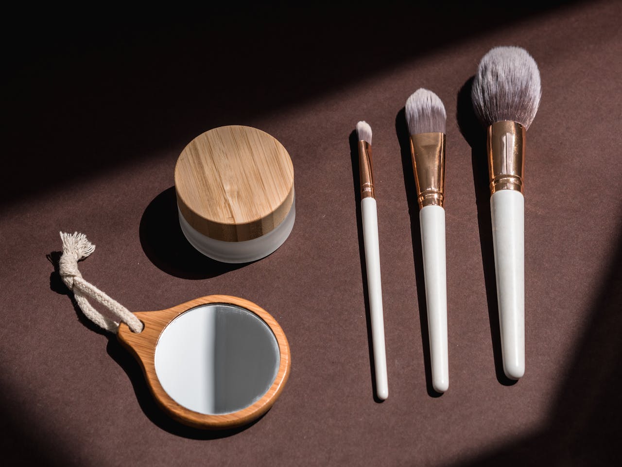 A chic display of wooden makeup brushes and a cosmetic jar on a dark surface.